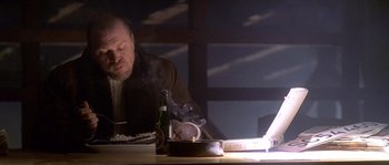 Movie still from “Flickering Lights” (2000), directed by Anders Thomas Jensen – A man sitting at a table with a bottle of wine; Medium shot, High angle