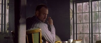 Movie still from “Flickering Lights” (2000), directed by Anders Thomas Jensen – A man smoking a cigarette while sitting at a table; Medium shot, Over the shoulder angle