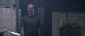 Movie still from “Flickering Lights” (2000), directed by Anders Thomas Jensen – A man standing in a dark room in front of a door; Medium shot, Low angle