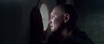 Movie still from “Flickering Lights” (2000), directed by Anders Thomas Jensen – A bald headed man looking into a round window; Close Up shot, Low angle