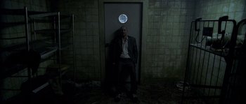 Movie still from “Flickering Lights” (2000), directed by Anders Thomas Jensen – A man standing in front of an open door; Wide shot, Low angle