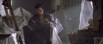 Movie still from “Flickering Lights” (2000), directed by Anders Thomas Jensen – A man sitting on a chair reading a book; Medium shot, Low angle
