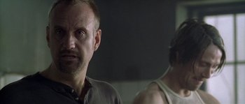 Movie still from “Flickering Lights” (2000), directed by Anders Thomas Jensen – A man standing next to another man in a dark room; Close Up shot, Over the shoulder angle
