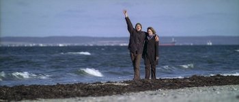 Movie still from “Flickering Lights” (2000), directed by Anders Thomas Jensen – A man and a woman standing next to each other on the beach; Wide shot, Low angle
