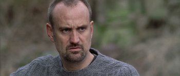 Movie still from “Flickering Lights” (2000), directed by Anders Thomas Jensen – A person wearing a sweater with trees in the background; Close Up shot, Low angle