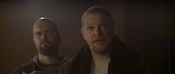 Movie still from “Flickering Lights” (2000), directed by Anders Thomas Jensen – A man with a goatee and a beard looking at the camera; Close Up shot, Low angle