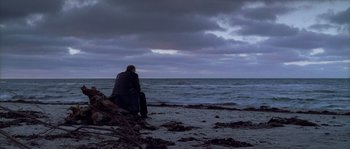 Movie still from “Flickering Lights” (2000), directed by Anders Thomas Jensen – A man sitting on the beach looking out at the ocean; Wide shot, Over the shoulder angle
