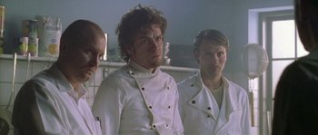 Movie still from “Flickering Lights” (2000), directed by Anders Thomas Jensen – A group of men standing next to each other in white coats; Medium shot, Low angle