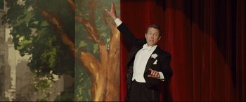 Movie still from “Florence Foster Jenkins” (2016), directed by Stephen Frears – A man in a tuxedo is holding his hand up in the air; Medium shot, Low angle