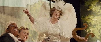 Movie still from “Florence Foster Jenkins” (2016), directed by Stephen Frears – An older woman dressed in a white dress and a feather headdress; Medium shot, Over the shoulder angle