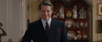 Movie still from “Florence Foster Jenkins” (2016), directed by Stephen Frears – A man in a suit and tie smiling for the camera; Close Up shot, Over the shoulder angle