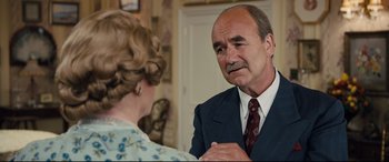 Movie still from “Florence Foster Jenkins” (2016), directed by Stephen Frears – An older man in a suit and tie talking to an older woman in a floral dress; Medium shot, Over the shoulder angle