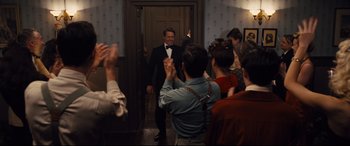 Movie still from “Florence Foster Jenkins” (2016), directed by Stephen Frears – A man in a suit and bow tie standing in front of a group of onlookers; Medium shot, Over the shoulder angle