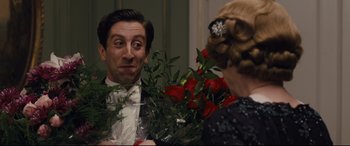 Movie still from “Florence Foster Jenkins” (2016), directed by Stephen Frears – A man and a woman holding roses in a room; Medium shot, Over the shoulder angle