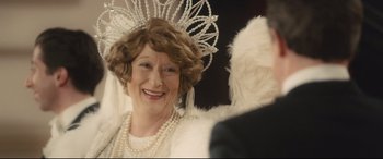 Movie still from “Florence Foster Jenkins” (2016), directed by Stephen Frears – An older woman wearing a tiara and a white feather boa; Close Up shot, Over the shoulder angle