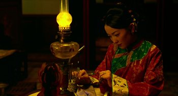 Movie still from “Flowers of Shanghai” (1998), directed by Hsiao-Hsien Hou – A woman in a red and black kimono is sitting in front of an oil lamp; Medium shot, High angle