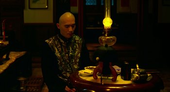 Movie still from “Flowers of Shanghai” (1998), directed by Hsiao-Hsien Hou – A man sitting in front of a table with a lamp on top of it; Medium shot, Low angle
