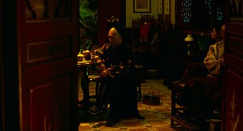 Movie still from “Flowers of Shanghai” (1998), directed by Hsiao-Hsien Hou – A man sitting at a dining room table with a wine glass; Wide shot, High angle