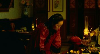 Movie still from “Flowers of Shanghai” (1998), directed by Hsiao-Hsien Hou – A woman in a red and black dress standing next to a table; Medium shot, High angle