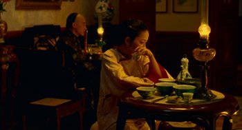 Movie still from “Flowers of Shanghai” (1998), directed by Hsiao-Hsien Hou – A woman sitting at a table with a bowl in front of her face; Medium shot, Over the shoulder angle