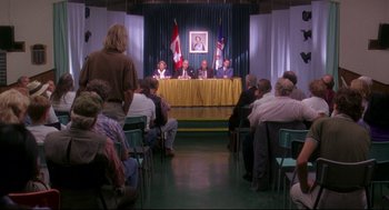 Movie still from “Fly Away Home” (1996), directed by Carroll Ballard – A group of people sitting in front of a microphone; Wide shot, High angle