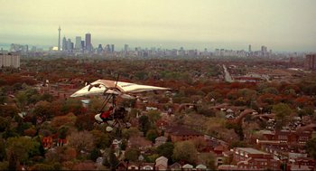 Movie still from “Fly Away Home” (1996), directed by Carroll Ballard – An aerial view of a city with a hang - glider in the foreground; Extreme Wide shot, High angle
