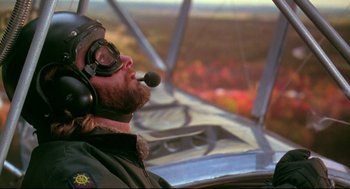 Movie still from “Fly Away Home” (1996), directed by Carroll Ballard – A man with a beard and glasses is sitting in the cockpit of an airplane; Medium shot, Low angle