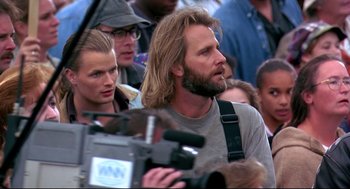 Movie still from “Fly Away Home” (1996), directed by Carroll Ballard – A man with long blond hair is standing next to a crowd of onlookers; Close Up shot, Over the shoulder angle