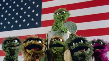 Movie still from “Follow That Bird” (1985), directed by Ken Kwapis – A group of green and brown puppets in front of an american flag; Medium shot, Low angle