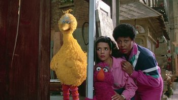 Movie still from “Follow That Bird” (1985), directed by Ken Kwapis – A group of people standing next to each other near a sesame street character; Medium shot, Low angle
