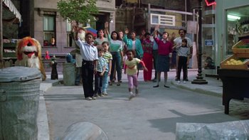 Movie still from “Follow That Bird” (1985), directed by Ken Kwapis – A group of people standing on a sidewalk; Wide shot, High angle
