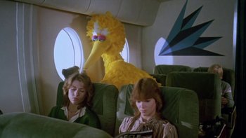 Movie still from “Follow That Bird” (1985), directed by Ken Kwapis – A big yellow bird sitting on top of an airplane next to two women; Medium shot, Low angle