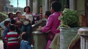 Movie still from “Follow That Bird” (1985), directed by Ken Kwapis – A group of people standing in a room; Medium shot, Low angle