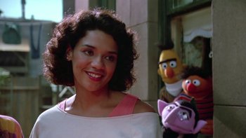 Movie still from “Follow That Bird” (1985), directed by Ken Kwapis – A young woman smiles in front of sesame street characters; Close Up shot, Low angle