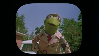 Movie still from “Follow That Bird” (1985), directed by Ken Kwapis – A man dressed as kermit the frog holding a microphone in front of a car; Medium shot, Low angle
