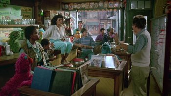 Movie still from “Follow That Bird” (1985), directed by Ken Kwapis – A group of people sitting around a room; Wide shot, Over the shoulder angle