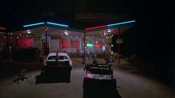 Movie still from “Follow That Bird” (1985), directed by Ken Kwapis – Two cars are parked in front of a gas station; Extreme Wide shot, Low angle