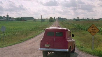 Movie still from “Follow That Bird” (1985), directed by Ken Kwapis – An old red truck driving down a dirt road; Extreme Wide shot, High angle