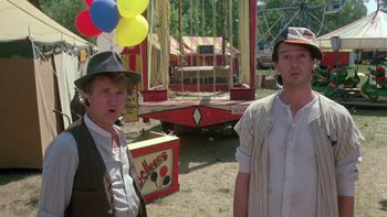 Movie still from “Follow That Bird” (1985), directed by Ken Kwapis – Two men standing next to each other in front of an amusement ride; Medium shot, Low angle