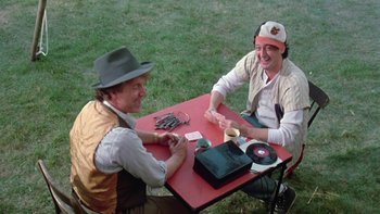 Movie still from “Follow That Bird” (1985), directed by Ken Kwapis – Two men sitting at a red table playing cards; Medium shot, Over the shoulder angle