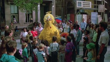 Movie still from “Follow That Bird” (1985), directed by Ken Kwapis – A group of people gathered around a big yellow bird costume; Extreme Wide shot, High angle