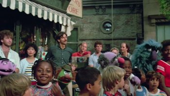 Movie still from “Follow That Bird” (1985), directed by Ken Kwapis – A group of people standing around a crowd of people; Medium shot, Over the shoulder angle