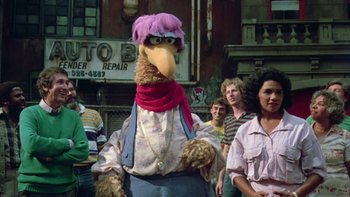Movie still from “Follow That Bird” (1985), directed by Ken Kwapis – A person dressed as a bird in front of a group of onlookers; Medium shot, Over the shoulder angle