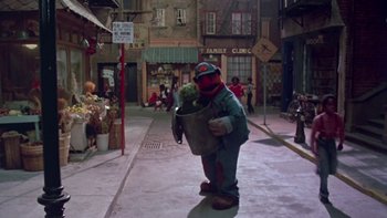 Movie still from “Follow That Bird” (1985), directed by Ken Kwapis – A person in a costume holding a metal bucket; Wide shot, High angle