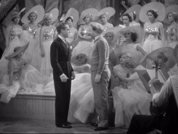 Movie still from “Footlight Parade” (1933), directed by Lloyd Bacon – A couple of men standing next to each other on a stage; Wide shot, High angle