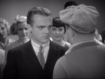 Movie still from “Footlight Parade” (1933), directed by Lloyd Bacon – A group of people standing around a man in a suit and tie; Close Up shot, Over the shoulder angle