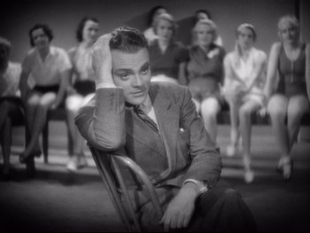Movie still from “Footlight Parade” (1933), directed by Lloyd Bacon – A man sitting in front of a group of women; Medium shot, High angle