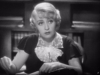 Movie still from “Footlight Parade” (1933), directed by Lloyd Bacon – An old photo of a woman sitting in front of a book shelf; Close Up shot, High angle