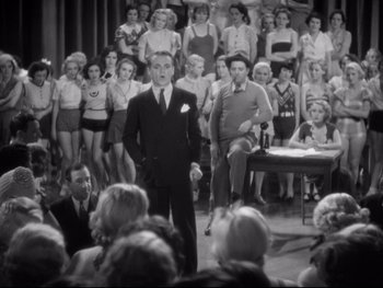 Movie still from “Footlight Parade” (1933), directed by Lloyd Bacon – An old photo of a man in front of a crowd; Wide shot, High angle