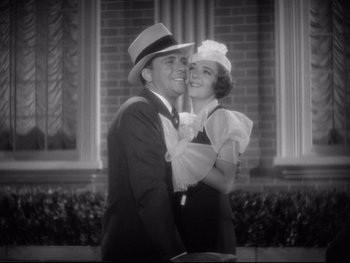 Movie still from “Footlight Parade” (1933), directed by Lloyd Bacon – A man and a woman embracing each other in front of a brick building; Medium shot, Low angle